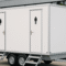 Een witte mobiele toiletwagen voor 8 personen met aparte deuren voor dames en heren, geplaatst op een evenementenlocatie